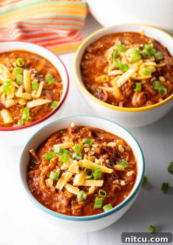 Three perfectly portioned bowls of vibrant chicken chili, each artfully garnished with a sprinkle of chopped green onions and a generous heap of shredded cheddar cheese, ready to be enjoyed.