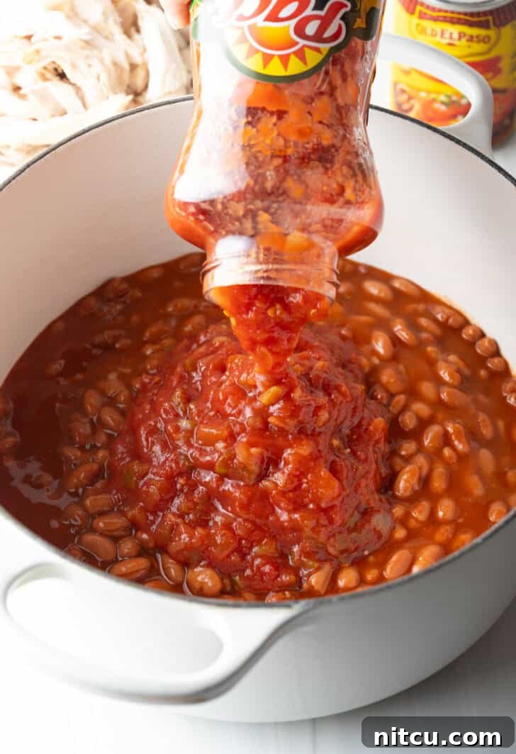 A vibrant red enchilada sauce being poured into the pot, mingling with the pinto beans and creating a rich, aromatic foundation for the chili, capturing the essence of the 5-ingredient simplicity.