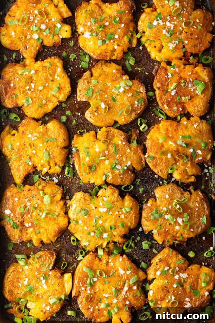 Top down view of 15 golden smashed potatoes on a baking sheet.