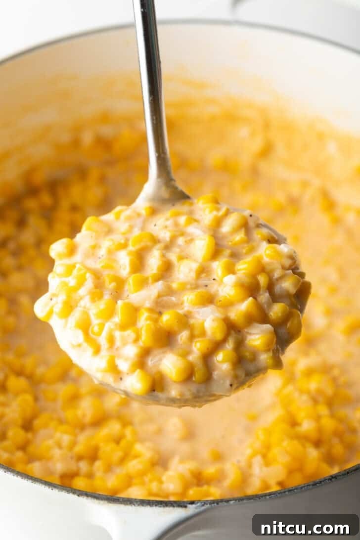 Ladleful of homemade creamed corn held to camera, showcasing its creamy texture and golden kernels.