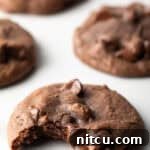 5 baked nutella cookies with chocolate chips on a white background. The closest cookie has a bite taken out of it.