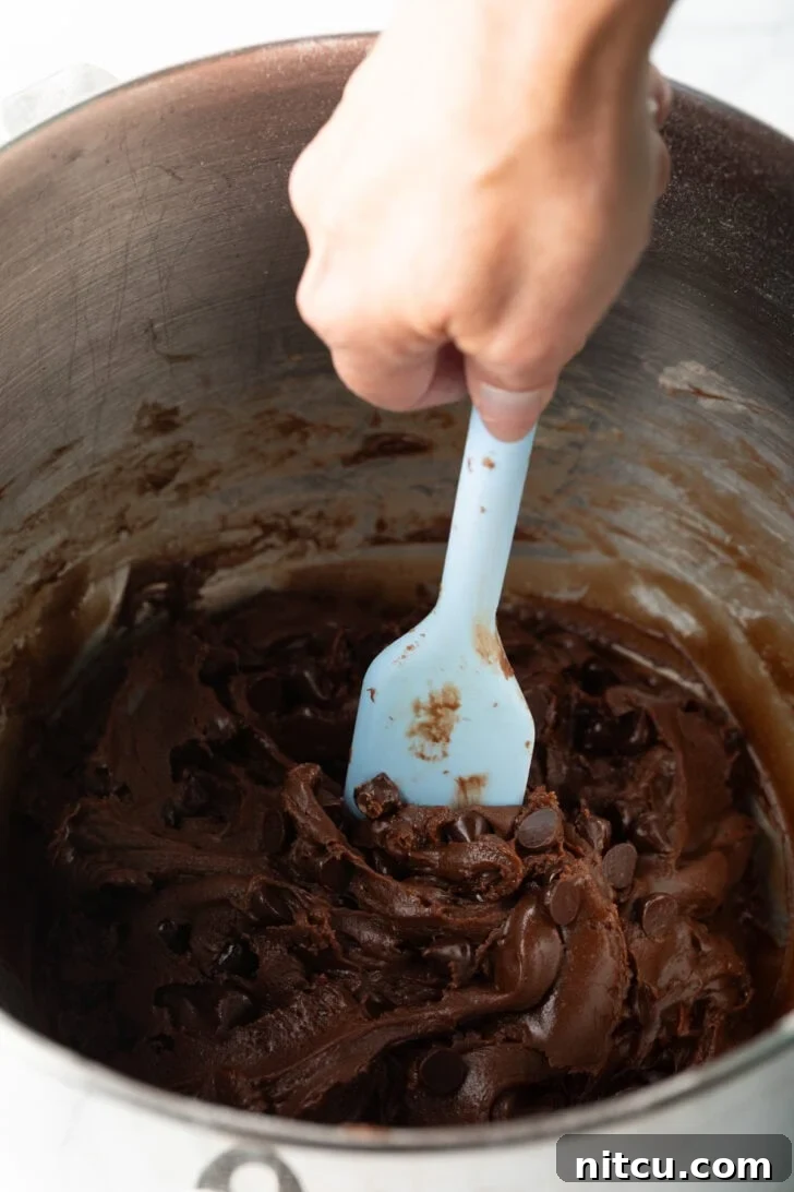 Using a blue spatula to combine nutella cookie ingredients in a large metal bowl.