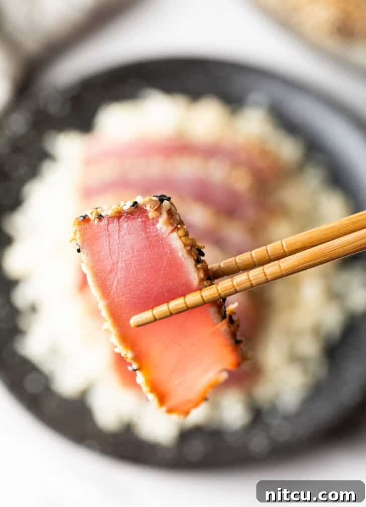 Close-up of a succulent slice of sesame-crusted seared yellowfin tuna held by chopsticks.