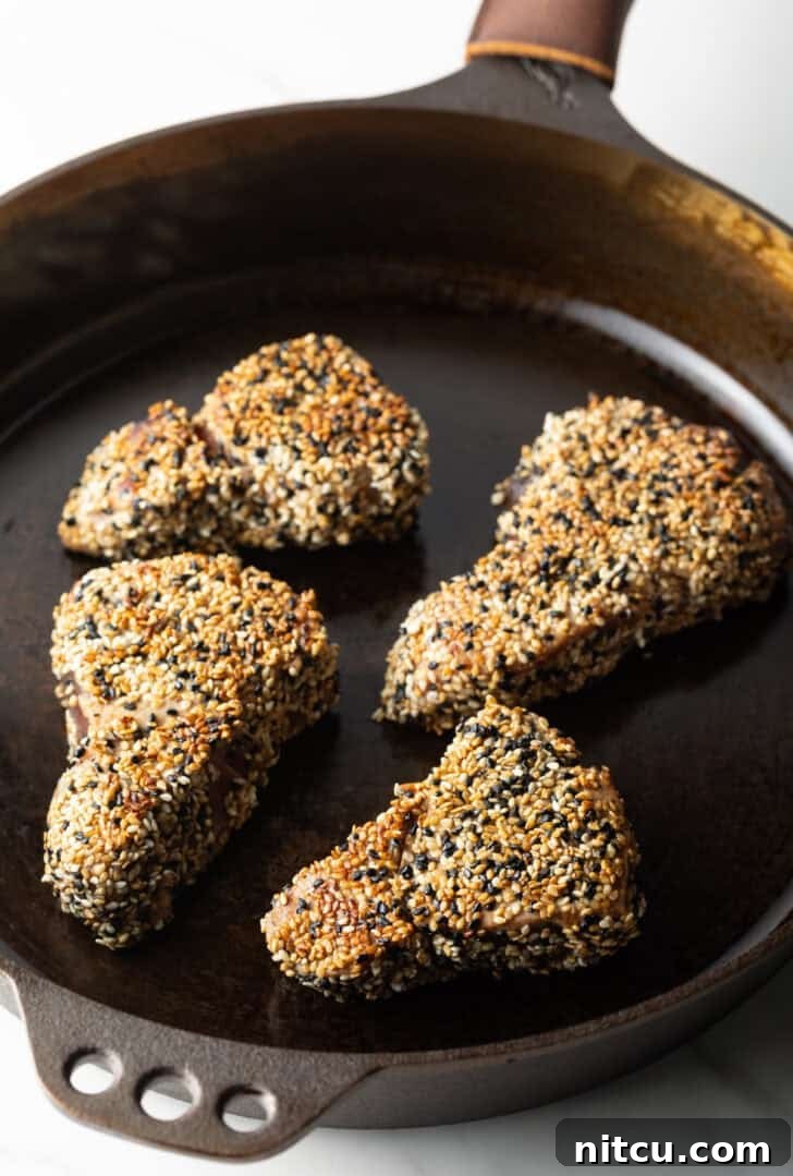 Four perfectly crusted yellowfin tuna steaks searing in a hot cast iron pan, forming a beautiful crust.