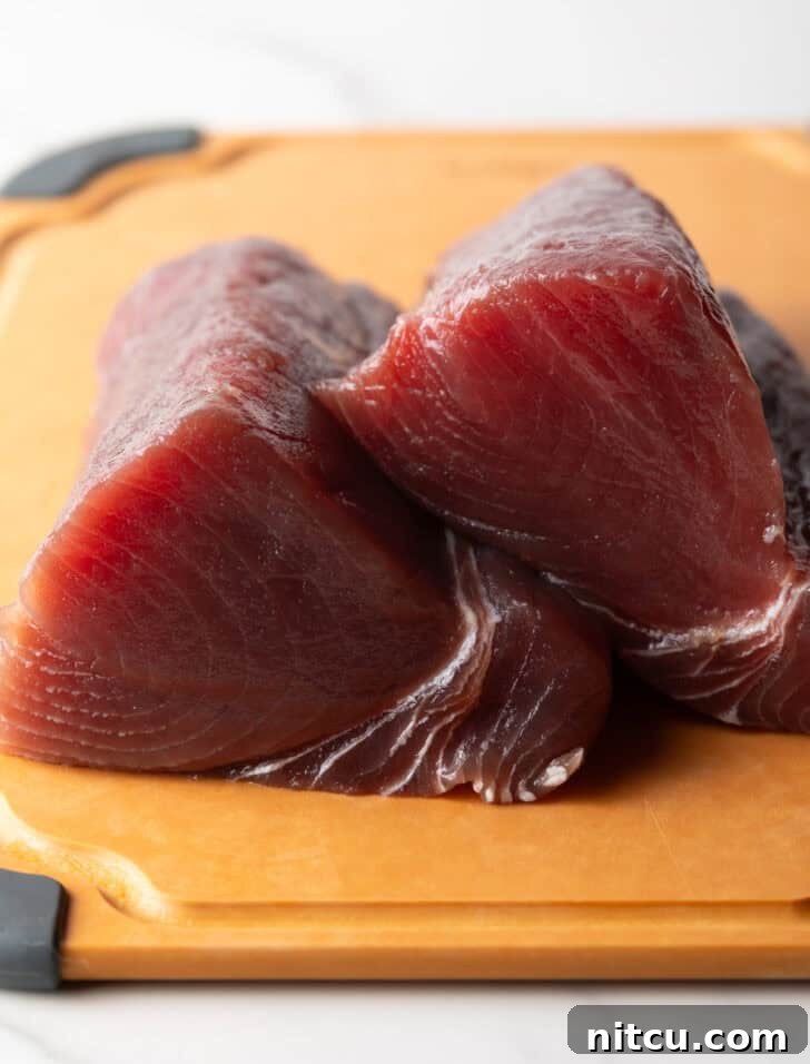 Two large pieces of raw yellowfin tuna on a cutting board, ready to be sliced.
