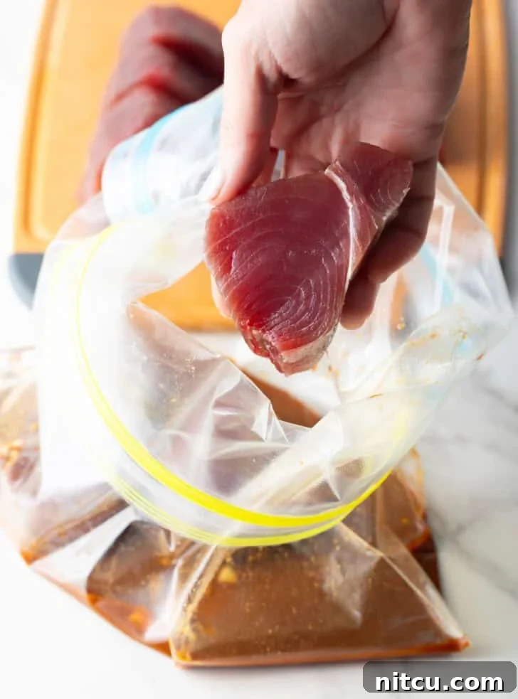 A hand carefully adding slices of yellowfin tuna to a plastic bag containing the marinade.