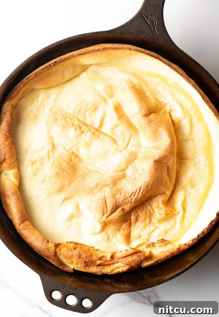 Top-down view of a beautifully baked Dutch Baby in a cast iron skillet, puffed high and golden.