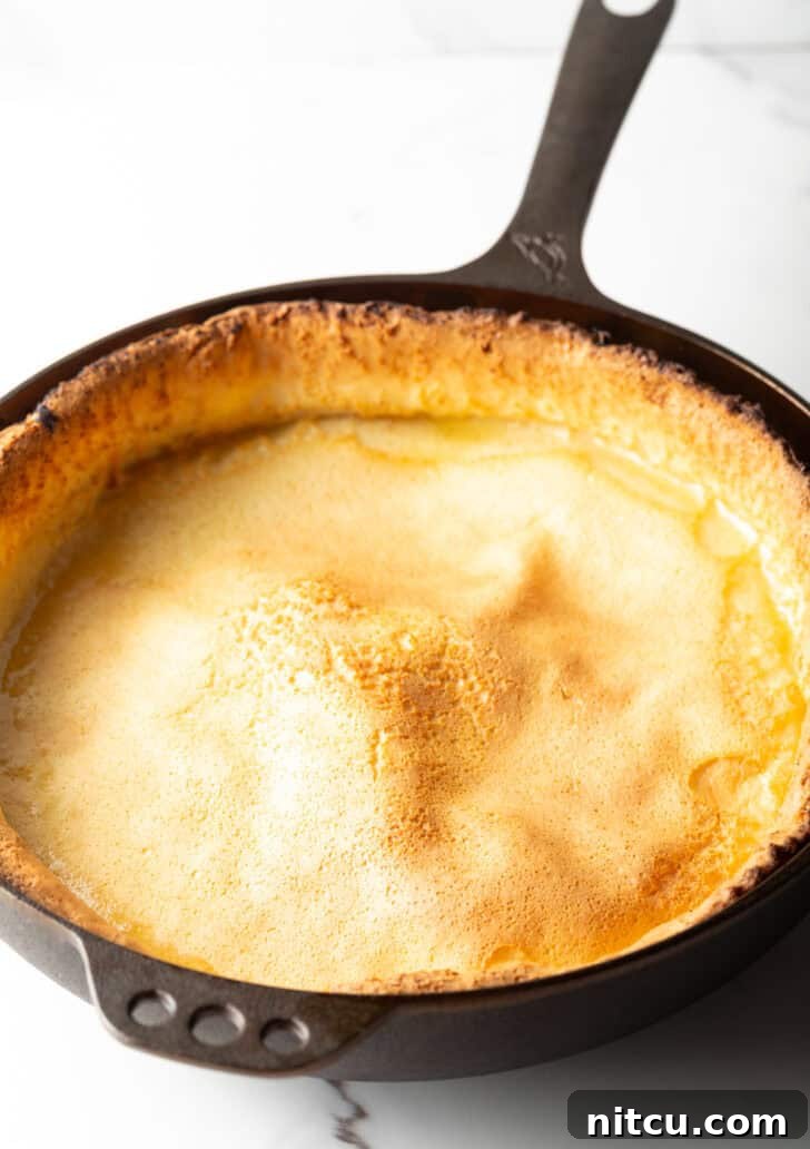 A freshly baked Dutch Baby in a cast iron skillet, slightly deflated but still beautiful, showcasing its crispy edges and soft center.