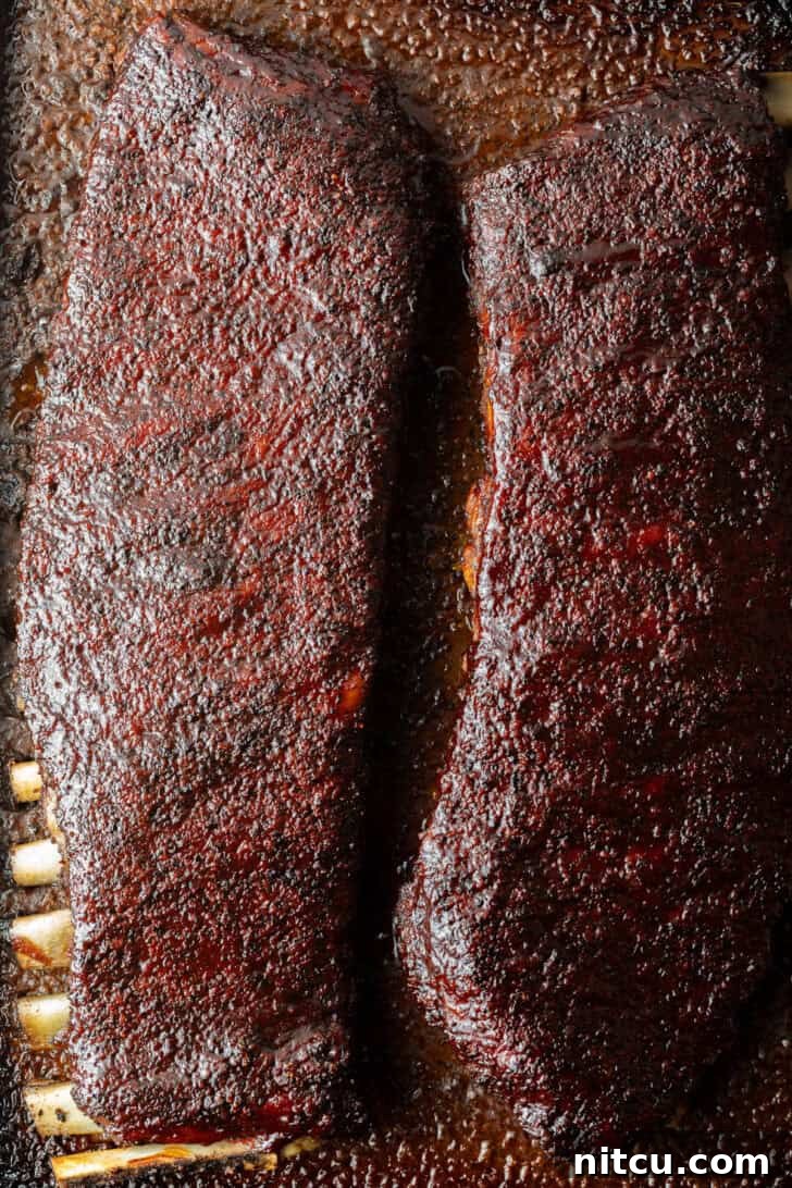 Two full racks of uncooked St. Louis pork ribs resting on a cooking tray.