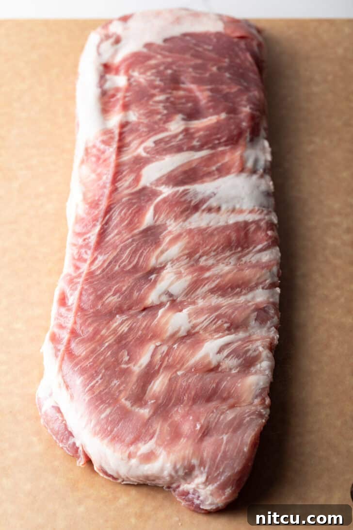 Overhead shot of a raw rack of pork ribs on a cutting board, ready for preparation.