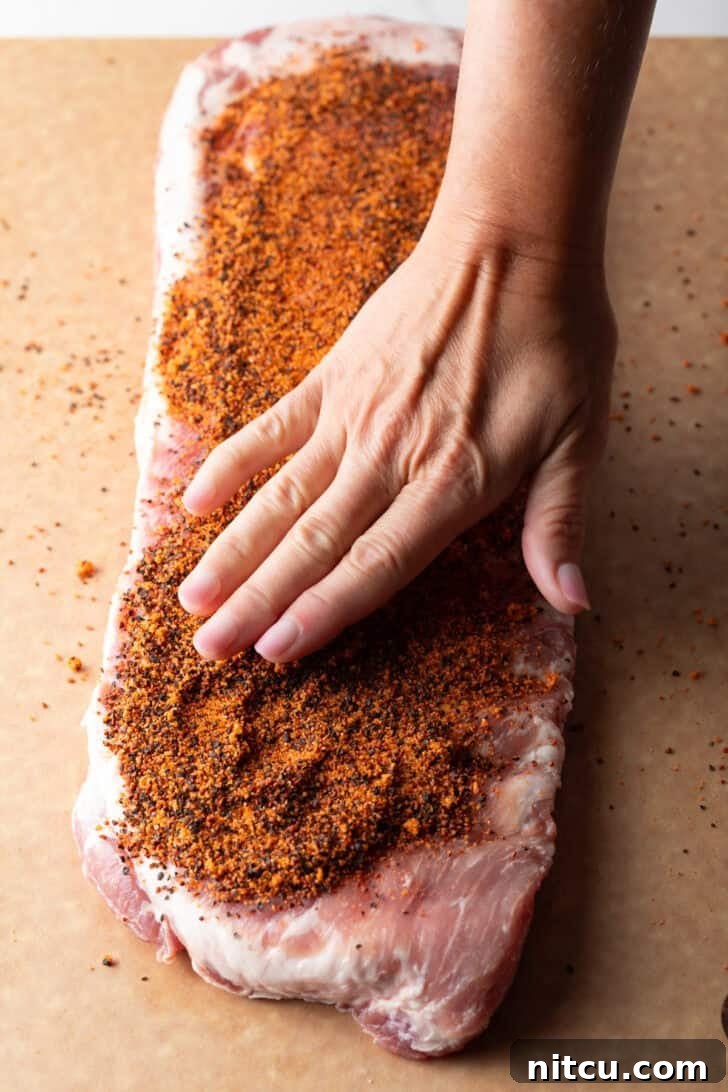 Overhead shot of a raw rack of pork ribs with a hand applying dry rub seasoning.