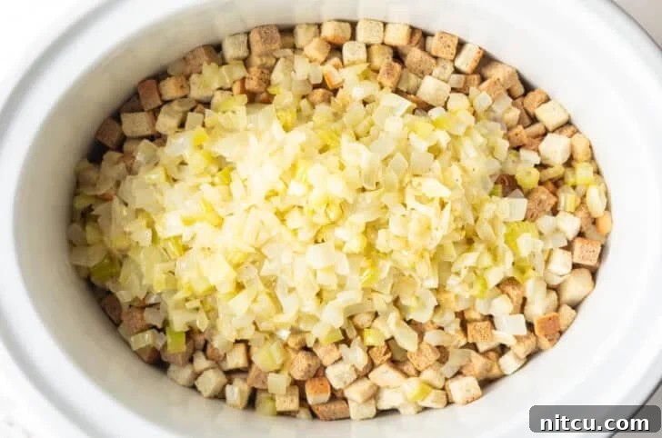 Dried bread cubes topped with cooked onions in a white crock pot.