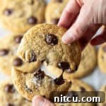 Close view of a hand breaking a chocolate chip cookie in half.