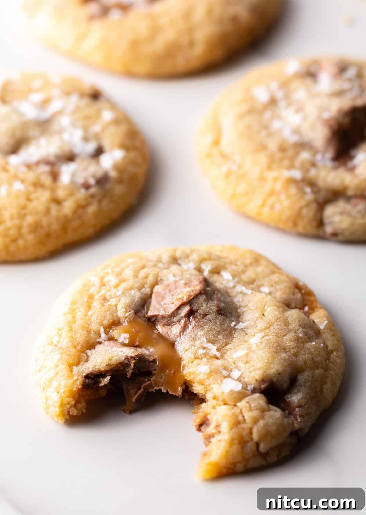 A Milky Way cookie on white surface with a bite taken out of it, revealing gooey caramel and nougat.