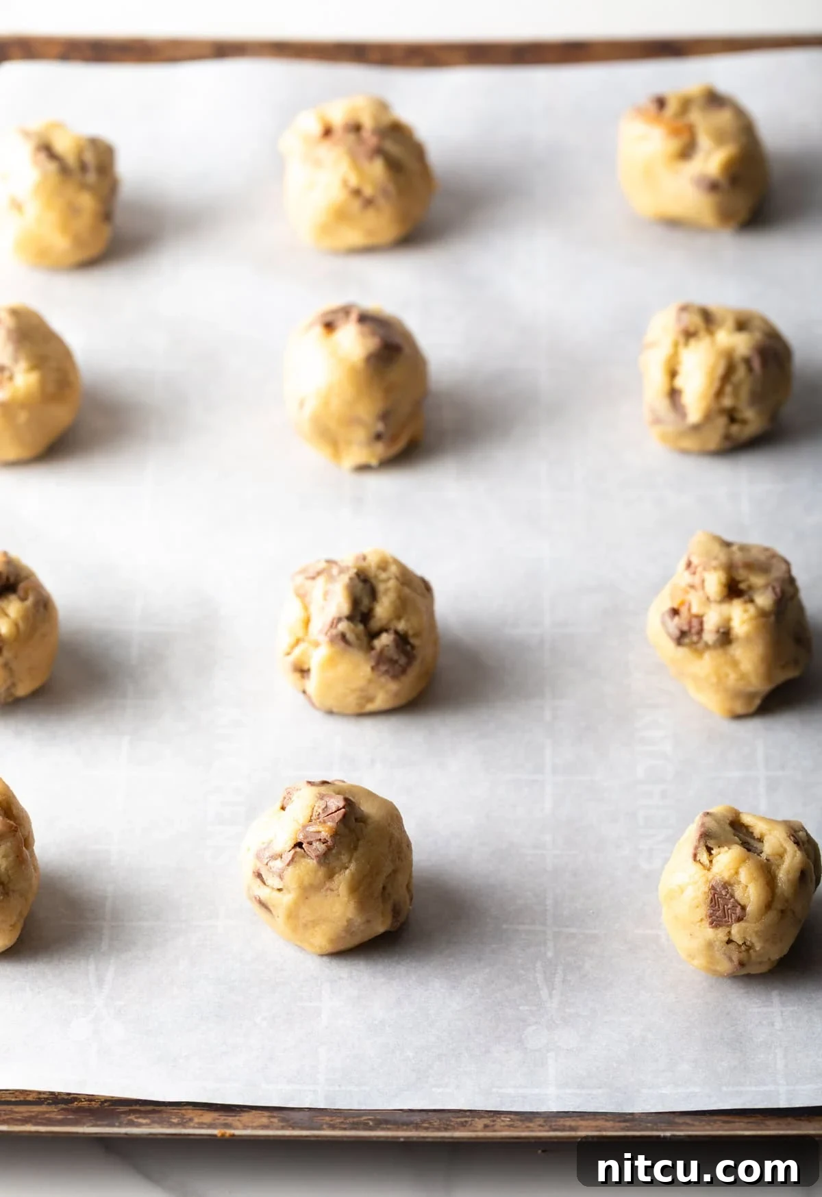 Milky Way Cookie dough rolled into balls on white parchment paper, perfectly spaced on a baking sheet.