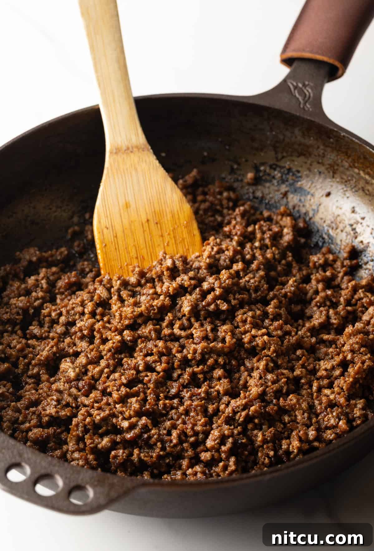 Cooking crumbled ground beef in a large skillet with a wooden spatula.