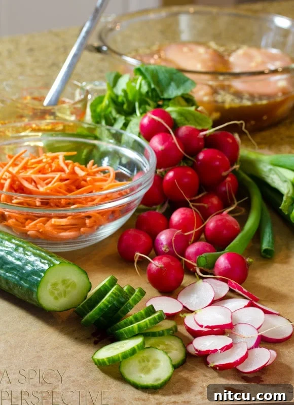 Recipe ingredients beautifully displayed: Whole and thinly sliced radishes, fresh sliced cucumber, vibrant whole green onions, and a glass bowl overflowing with finely shredded carrots. These are key components for a refreshing Banh Mi salad.