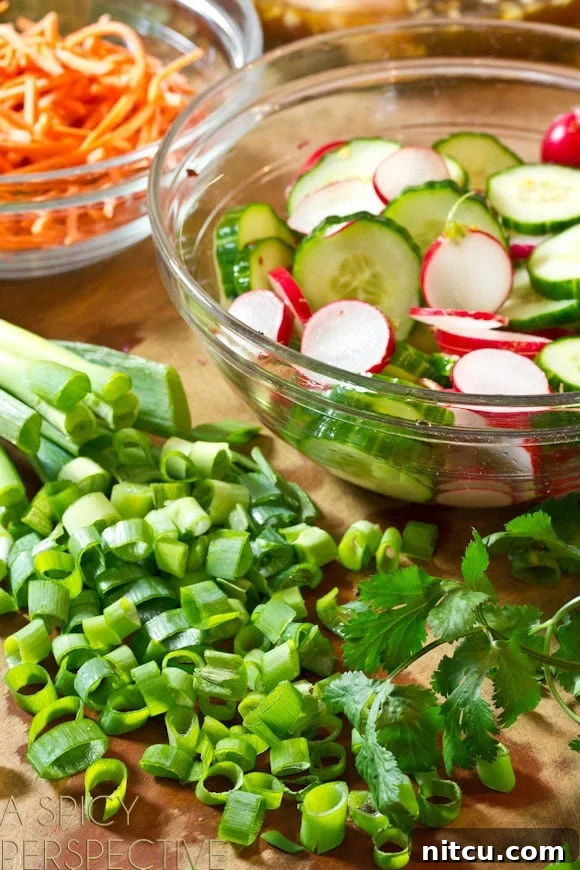 Close-up of freshly prepped ingredients for a Banh Mi salad: A neat pile of thinly sliced green onions and a clear glass bowl filled with perfectly sliced cucumbers and radishes soaking in a light pickling liquid. Ready for assembly!