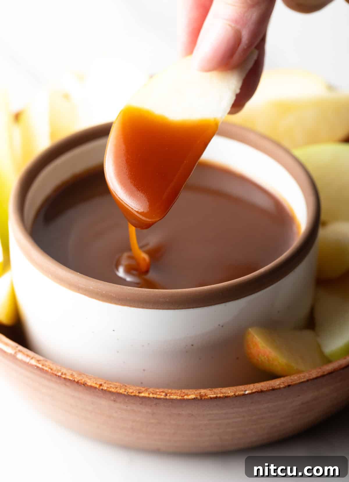 An apple slice being dipped into a container of salted caramel sauce.