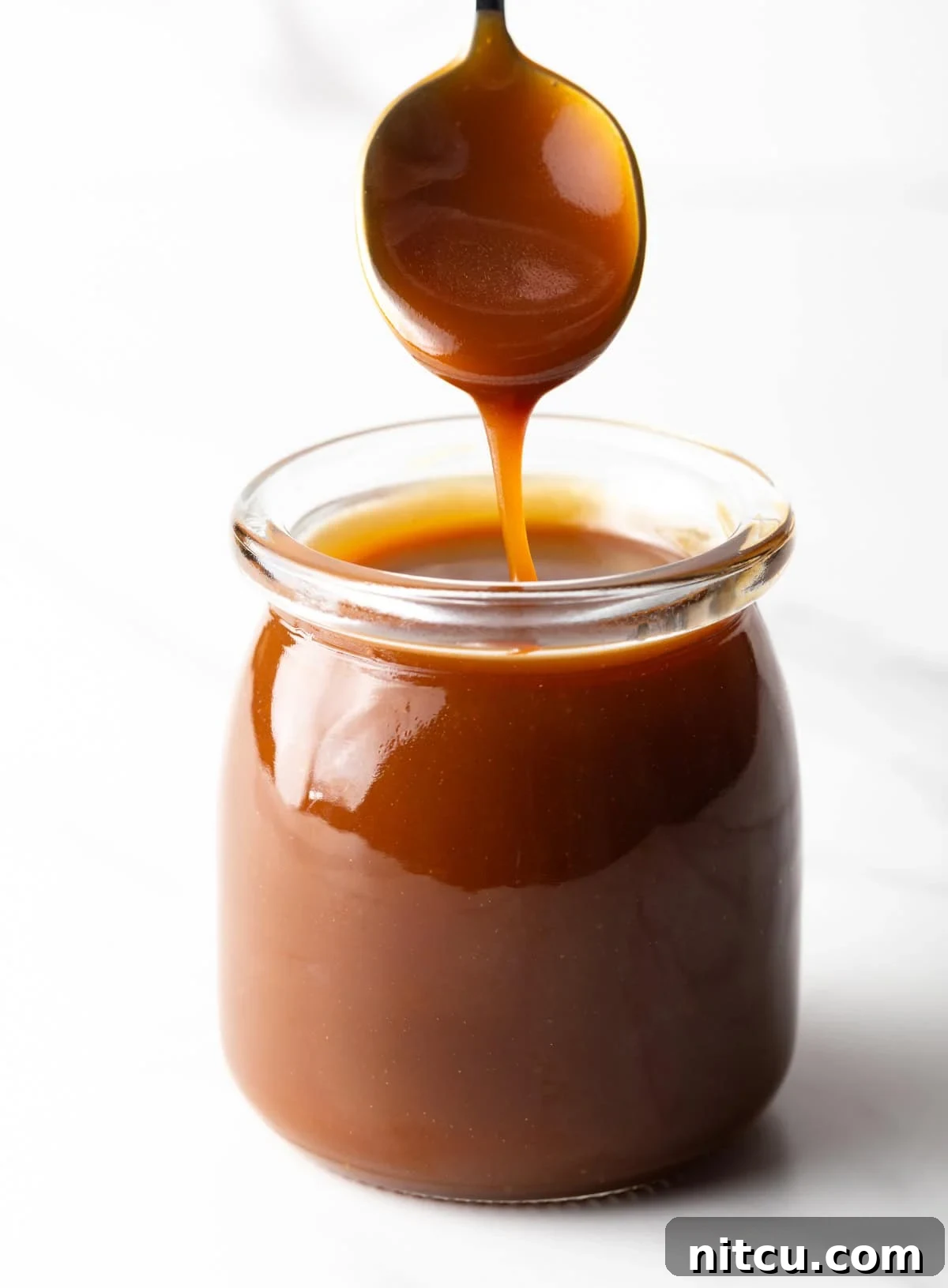 Homemade salted caramel sauce being drizzled with a spoon into a glass jar.