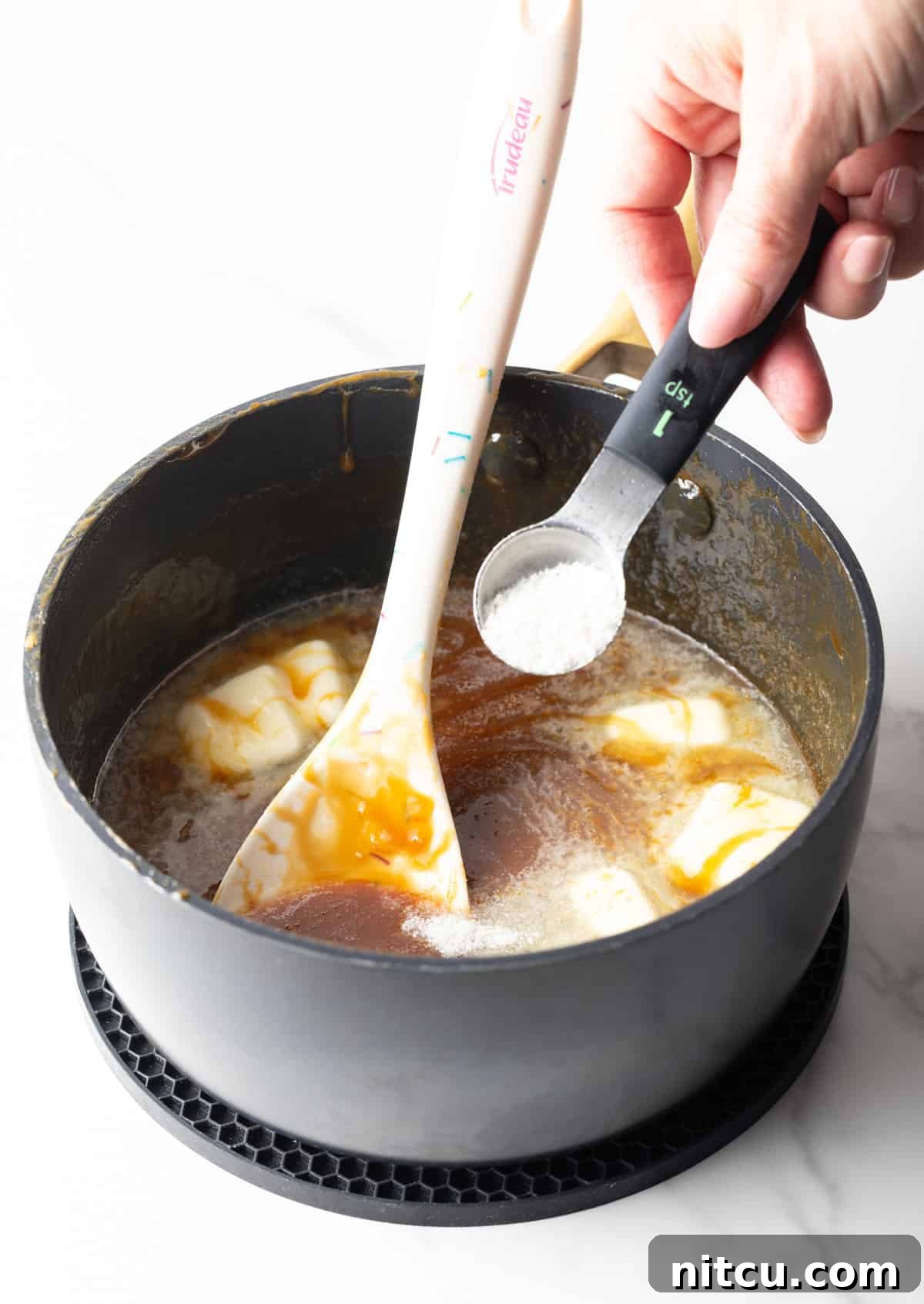 Ingredients being added to salted caramel sauce in a black sauce pan.