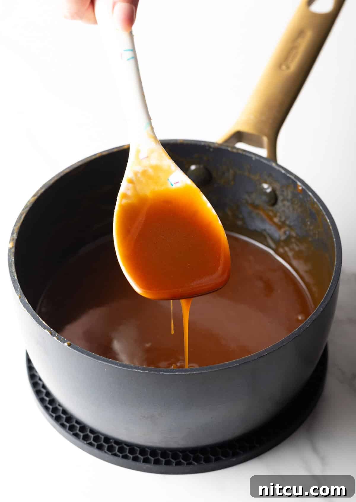 A white spatula holding salted caramel sauce over a black saucepan.