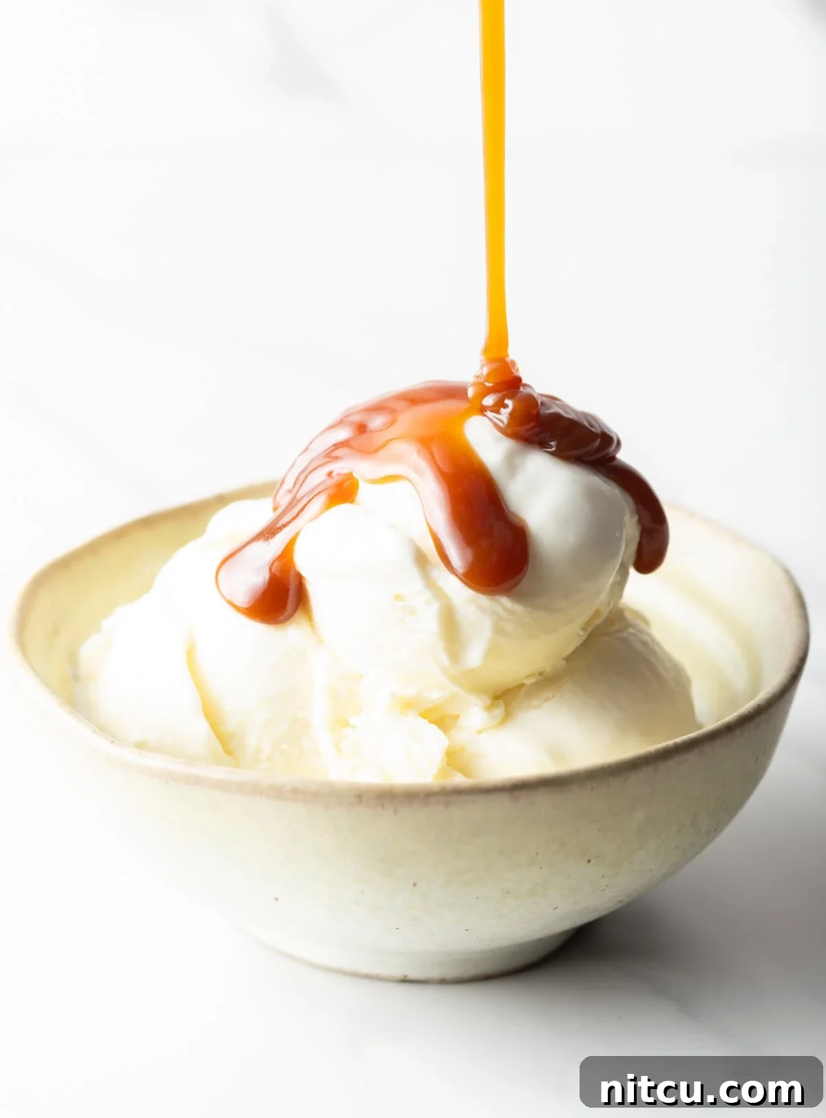 Salted caramel being drizzled over vanilla ice cream in a white bowl.