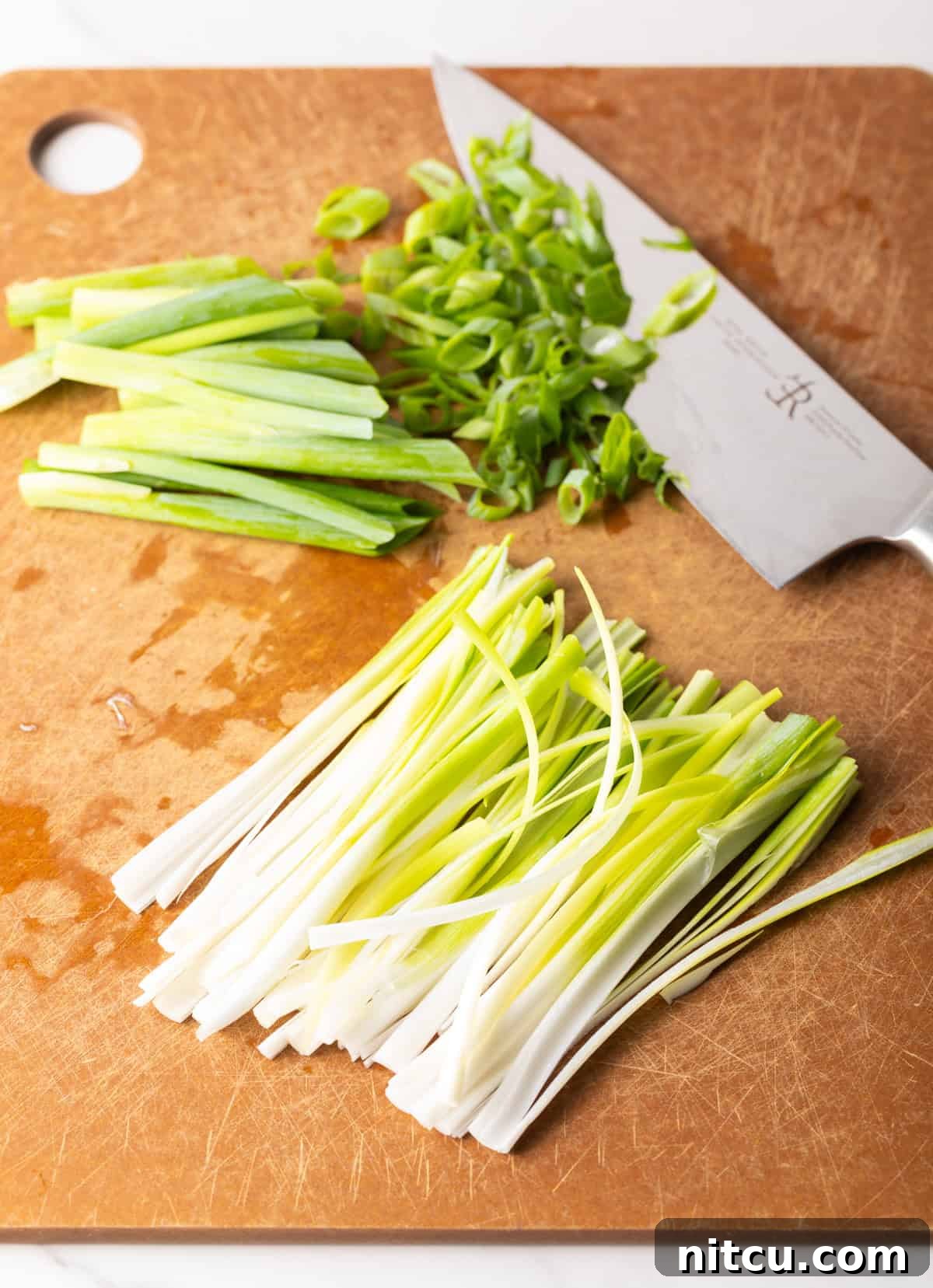 Chopped green onions on a cutting board next to a knife.