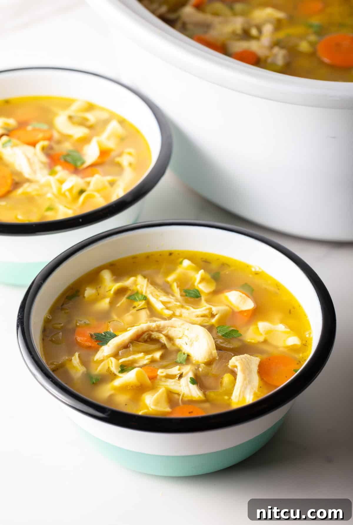 Two bowls of chicken noodle soup with generous portions of chicken, noodles, and vegetables.
