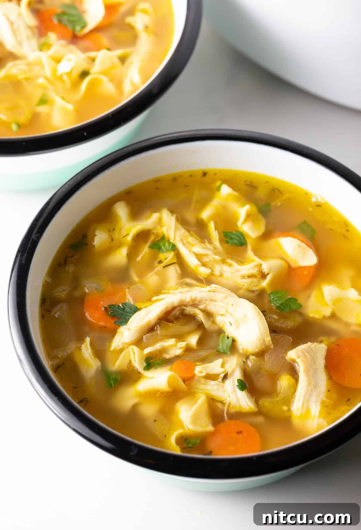 A bowl filled with homemade crockpot chicken noodle soup, garnished with fresh herbs.