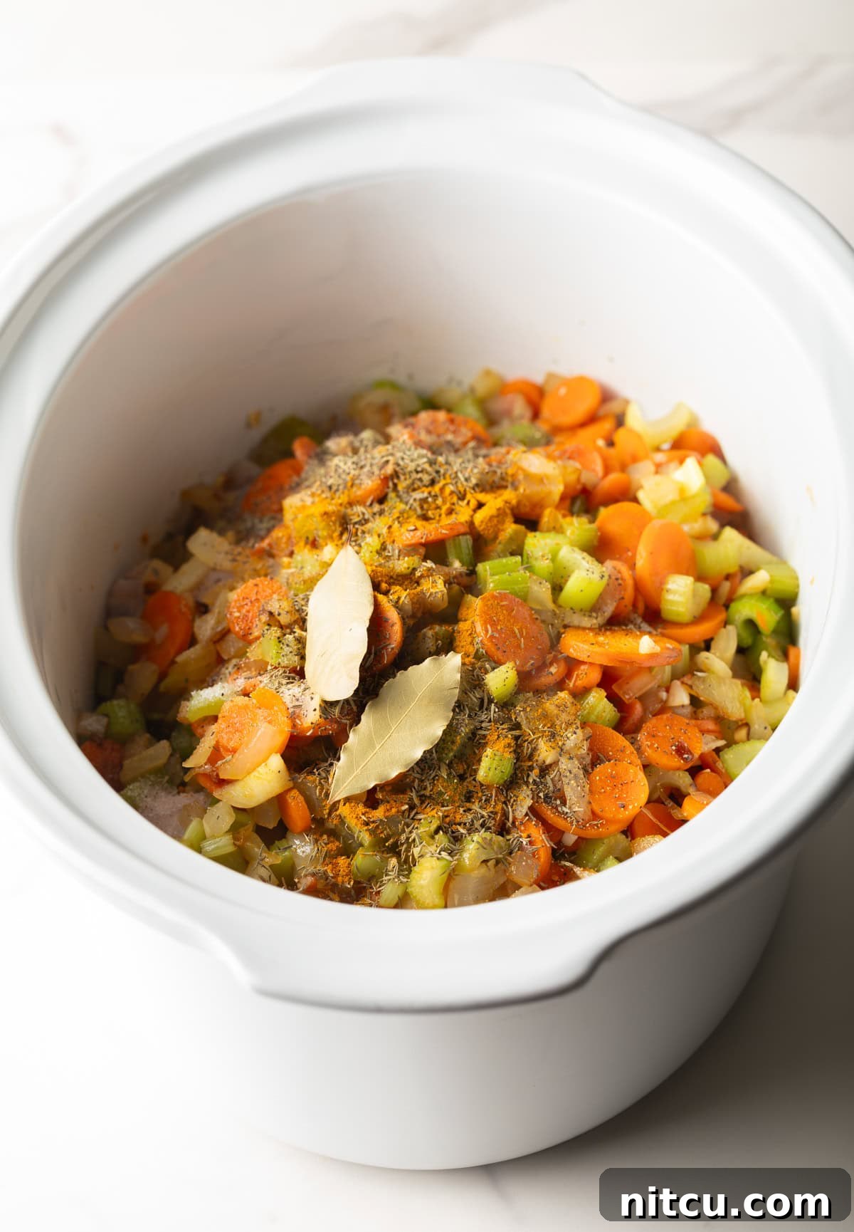 Overhead shot of vegetable mixture for crockpot chicken noodle soup sitting in a white crockpot.
