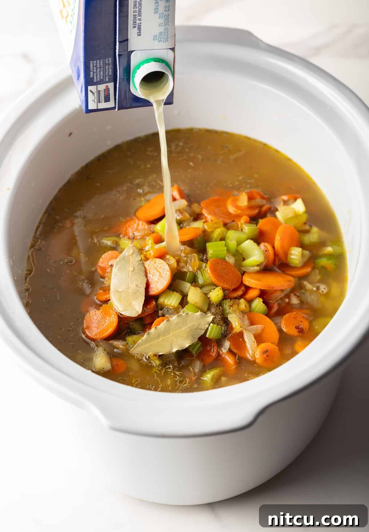 Overhead shot of chicken broth being poured over vegetable and chicken mixture in the crockpot.