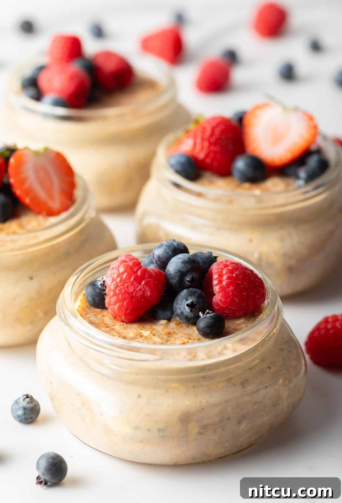 Small jars filled with high protein overnight oats topped with raspberries and blueberries.