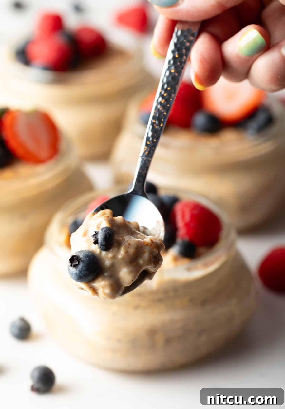 A spoon holding a bite of high protein oatmeal above a glass jar.