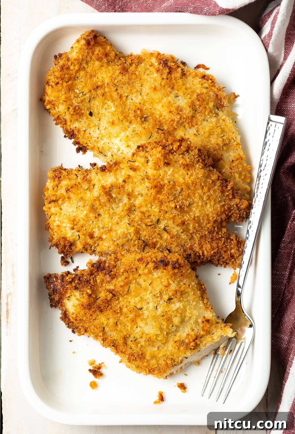 Overhead shot of oven fried chicken on a platter, garnished with fresh parsley and lemon wedges.