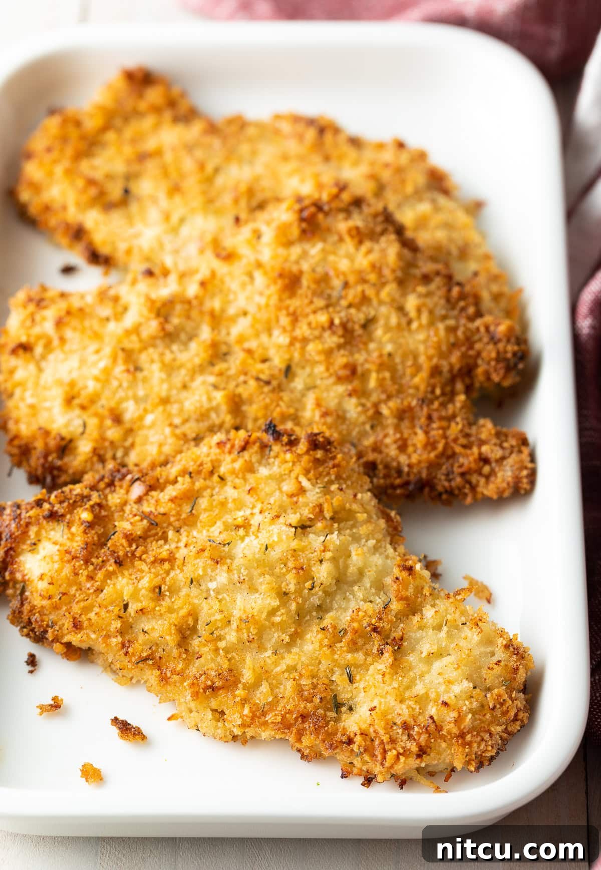 Close up of perfectly golden and crispy baked breaded chicken cutlets on a platter.