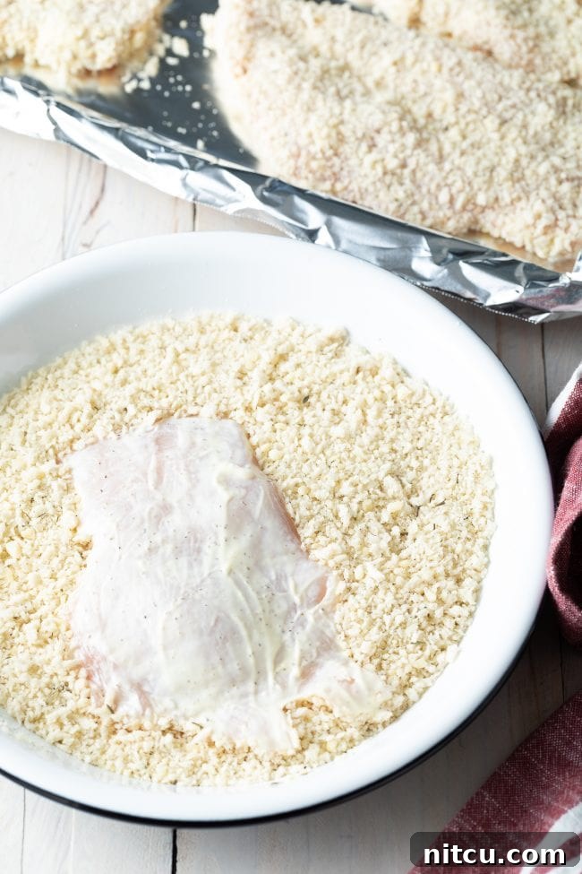 Mayo-coated chicken cutlet being carefully covered in the breadcrumb mixture, ensuring even coverage.