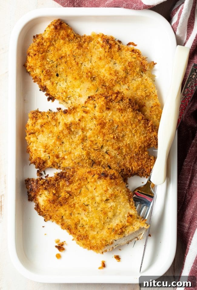 Plated cooked chicken cutlet with a fork and bite taken out, showing the juicy interior.