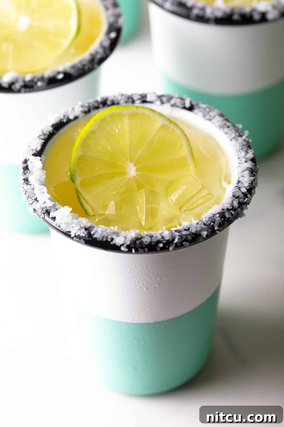 A white and green-striped cup with salt around the rim and a slice of lime in the drink.
