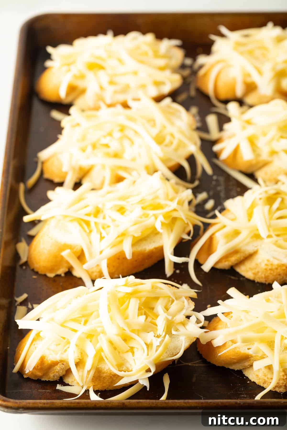A dozen golden-brown baguette slices, generously topped with melted and bubbly Gouda cheese, baked to perfection on a baking sheet, ready to be served.