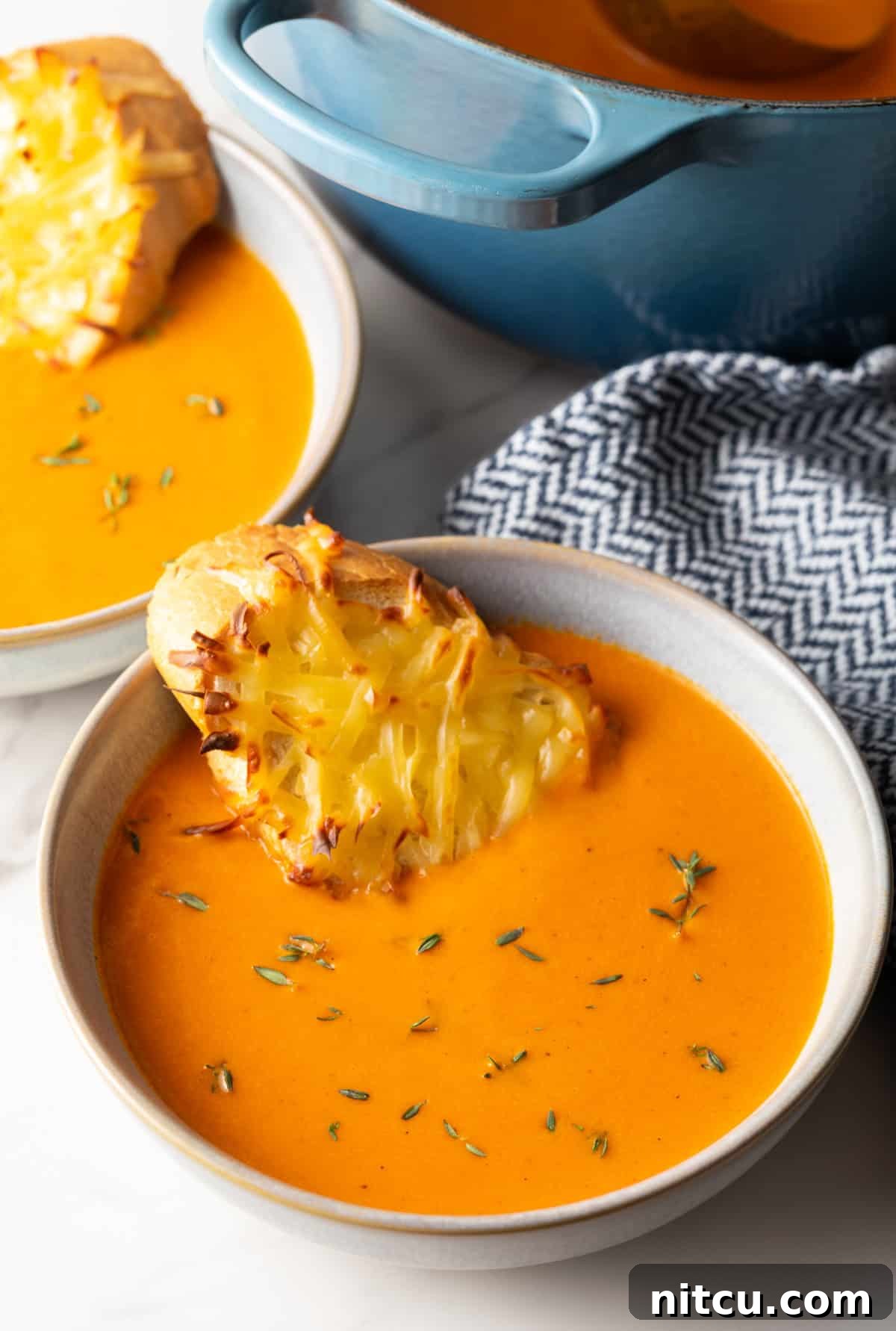 A beautifully presented bowl of creamy roasted red pepper Gouda soup, garnished with fresh herbs and a slice of cheesy baguette toast resting on the rim.