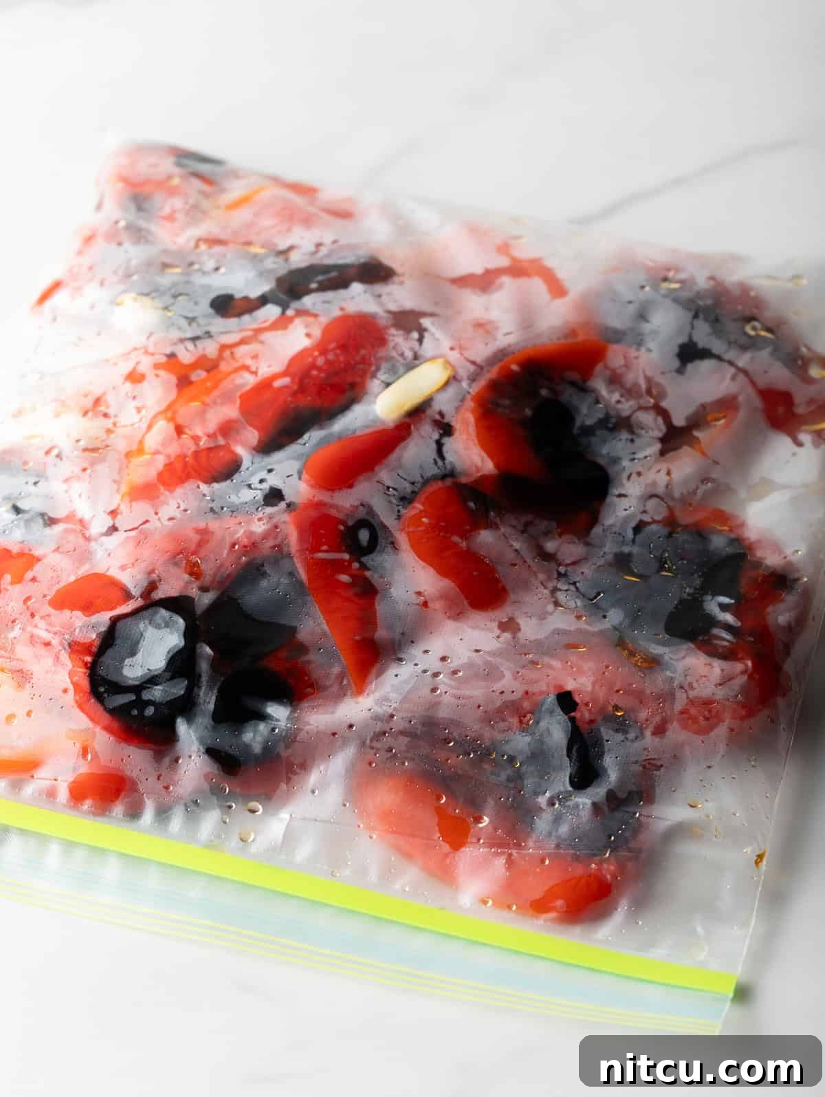 Charred red bell peppers captured inside a clear ziplock bag, steaming to loosen their skins for easy peeling, a crucial step for creamy roasted red pepper soup.