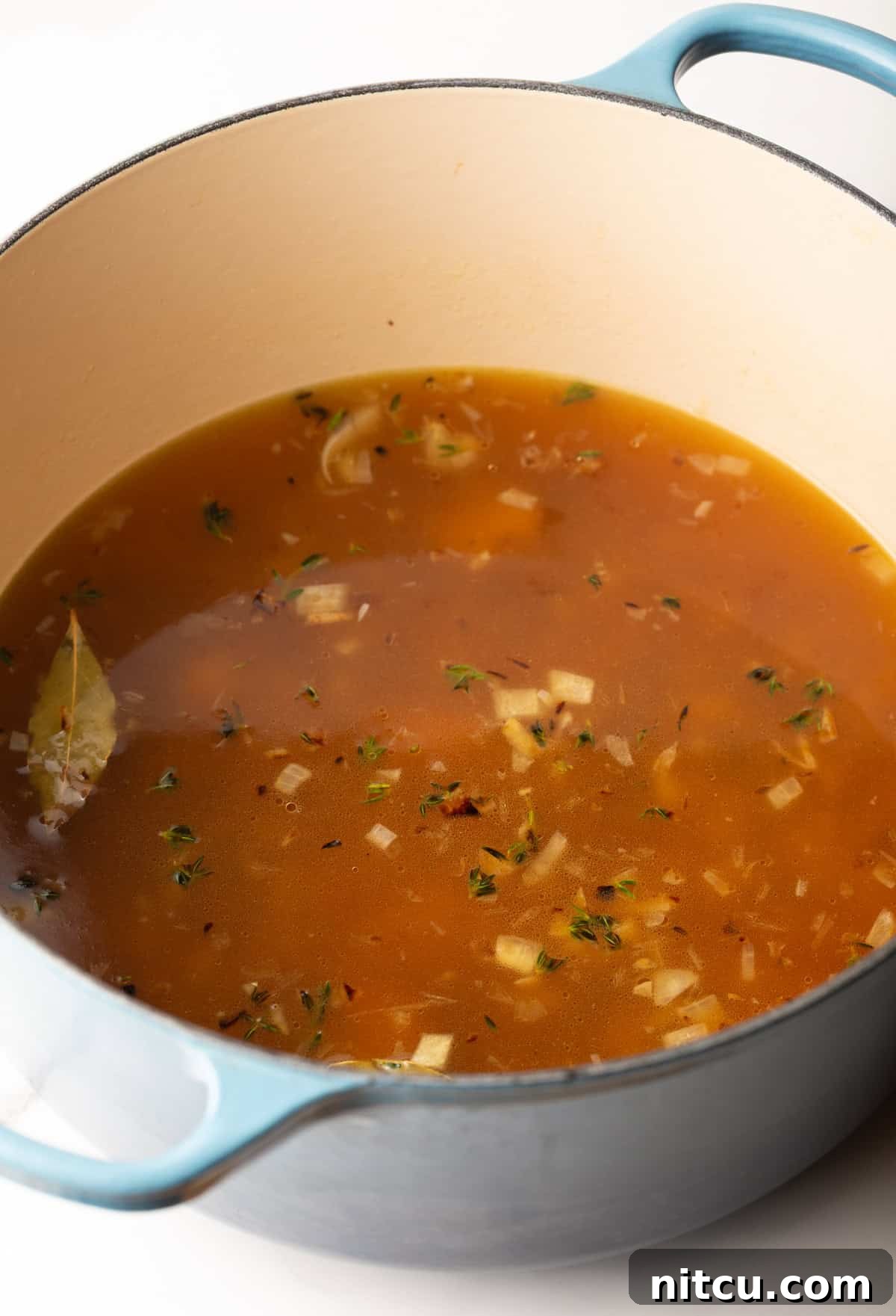 A large soup pot containing a simmering blend of onions, garlic, broth, tomato paste, and herbs, forming the aromatic base for the roasted red pepper Gouda soup.
