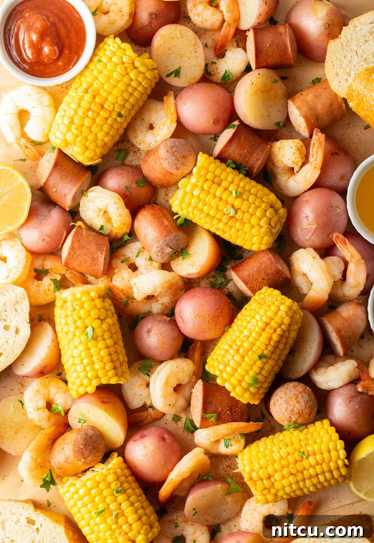 A vibrant display of fresh ingredients for a Low Country Boil, including raw shrimp, slices of smoked sausage, bright corn on the cob, and small red potatoes, all generously dusted with aromatic Old Bay seasoning, ready for cooking.