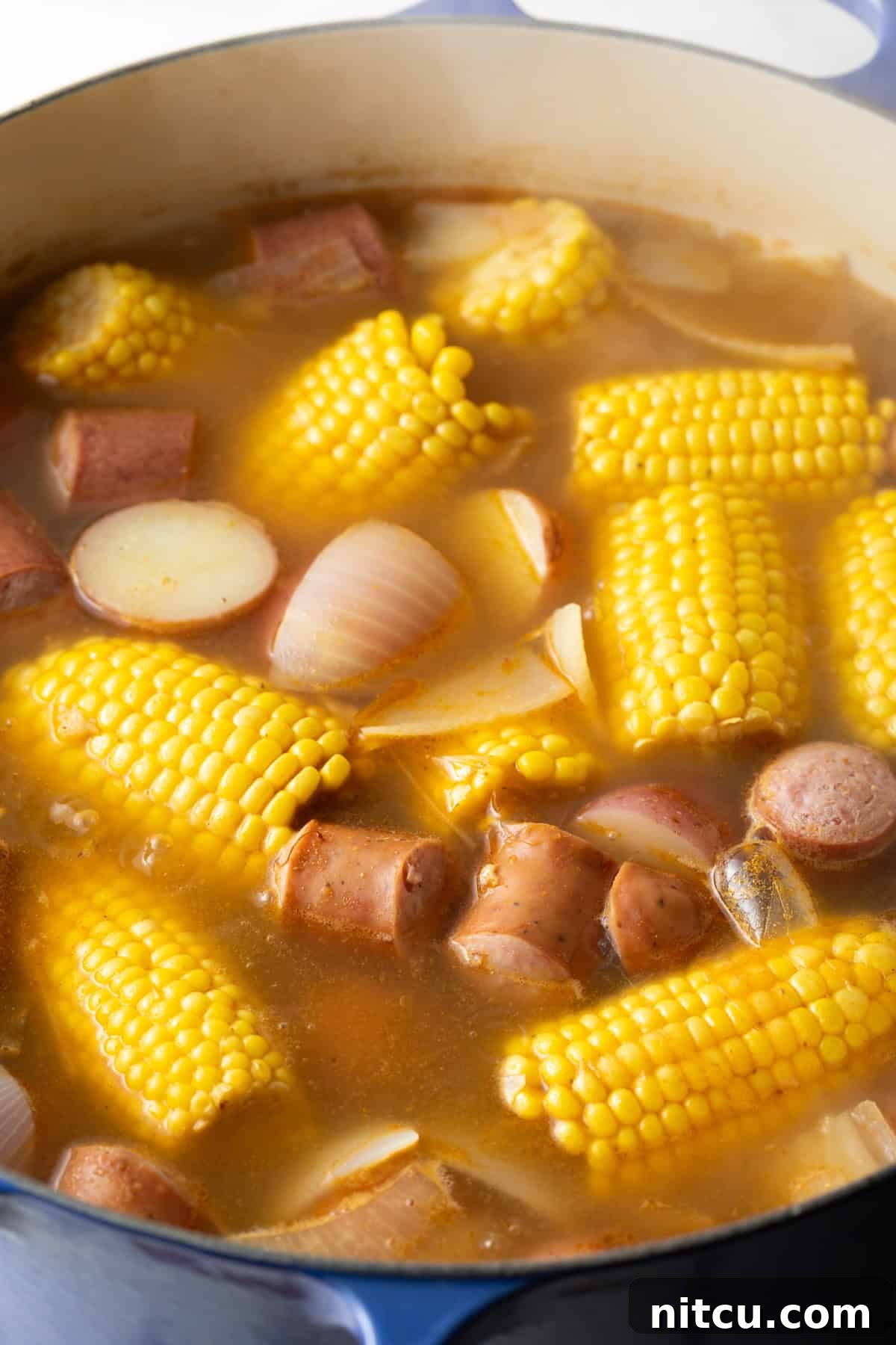 A bubbling pot brimming with the rich, Old Bay spiced broth, featuring vibrant yellow corn on the cob, tender red potatoes, savory onions, and smoky sausage, all simmering together.