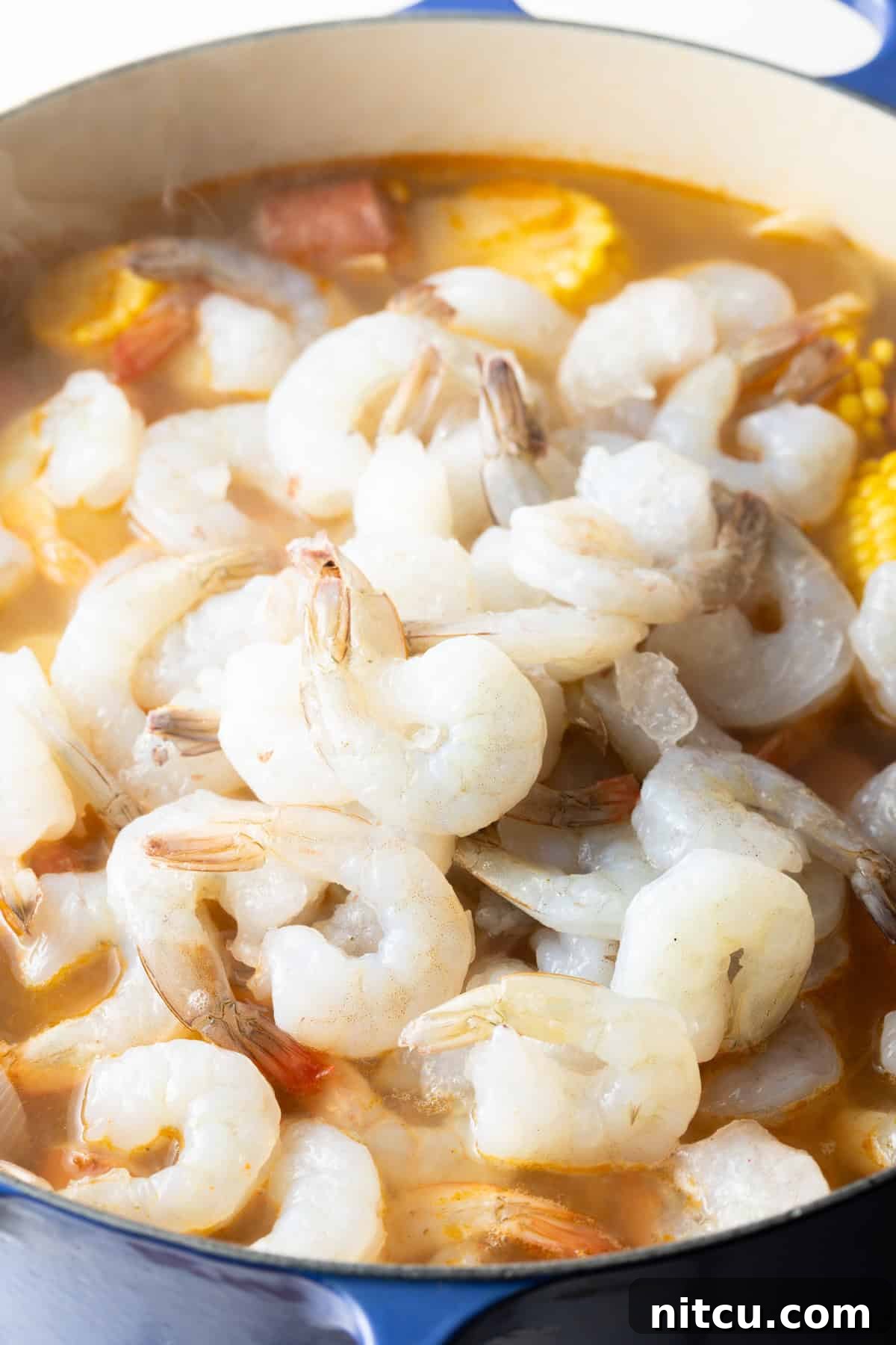 Fresh, raw shrimp are being carefully added to the vibrant pot of low country shrimp and sausage boil, ready to cook quickly and absorb the rich flavors.
