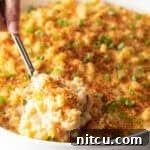 A spoon is scooping a serving of New Orleans style macaroni and cheese from a white dish.
