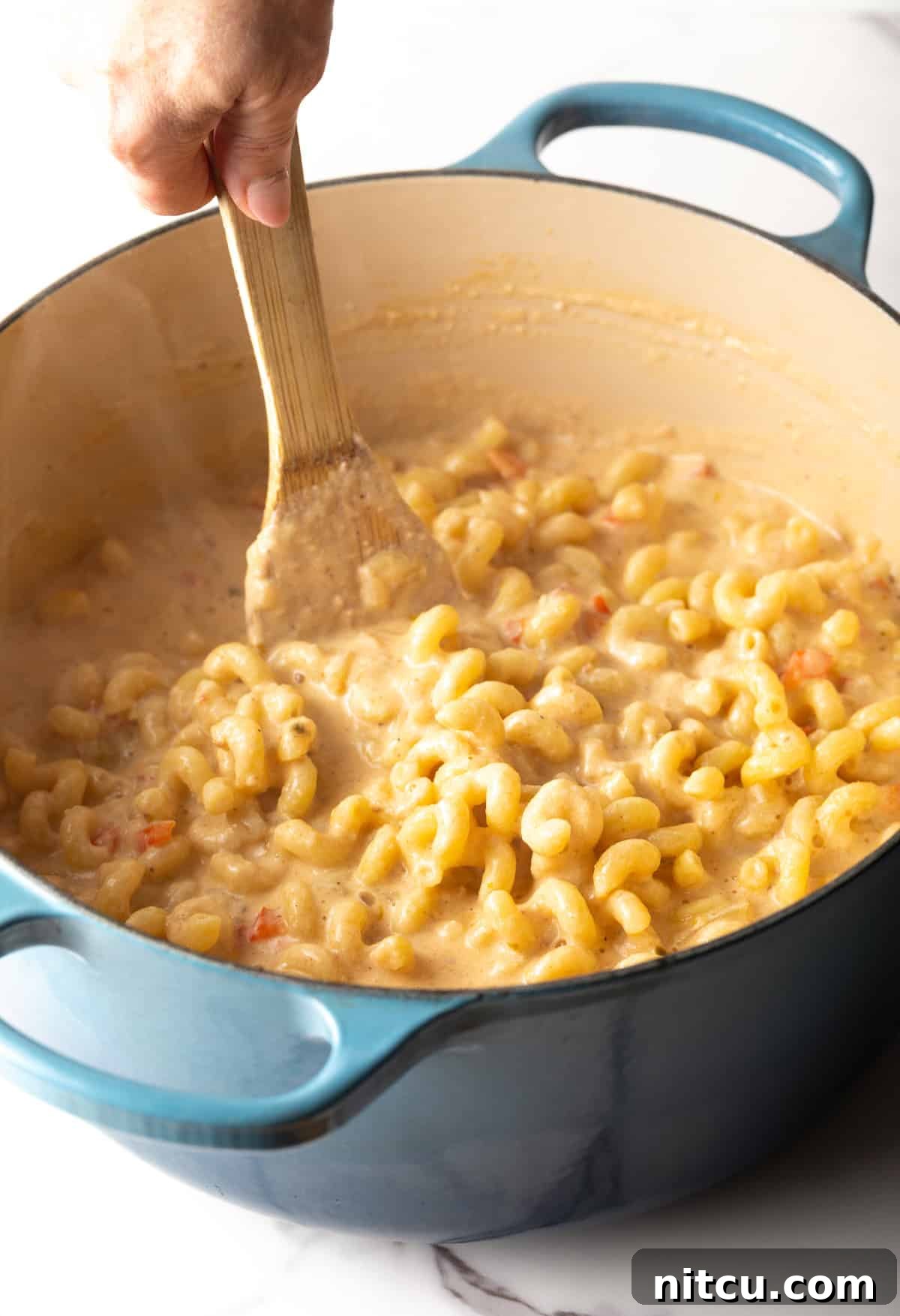 A wooden spoon is stirring pasta into the cheese sauce.