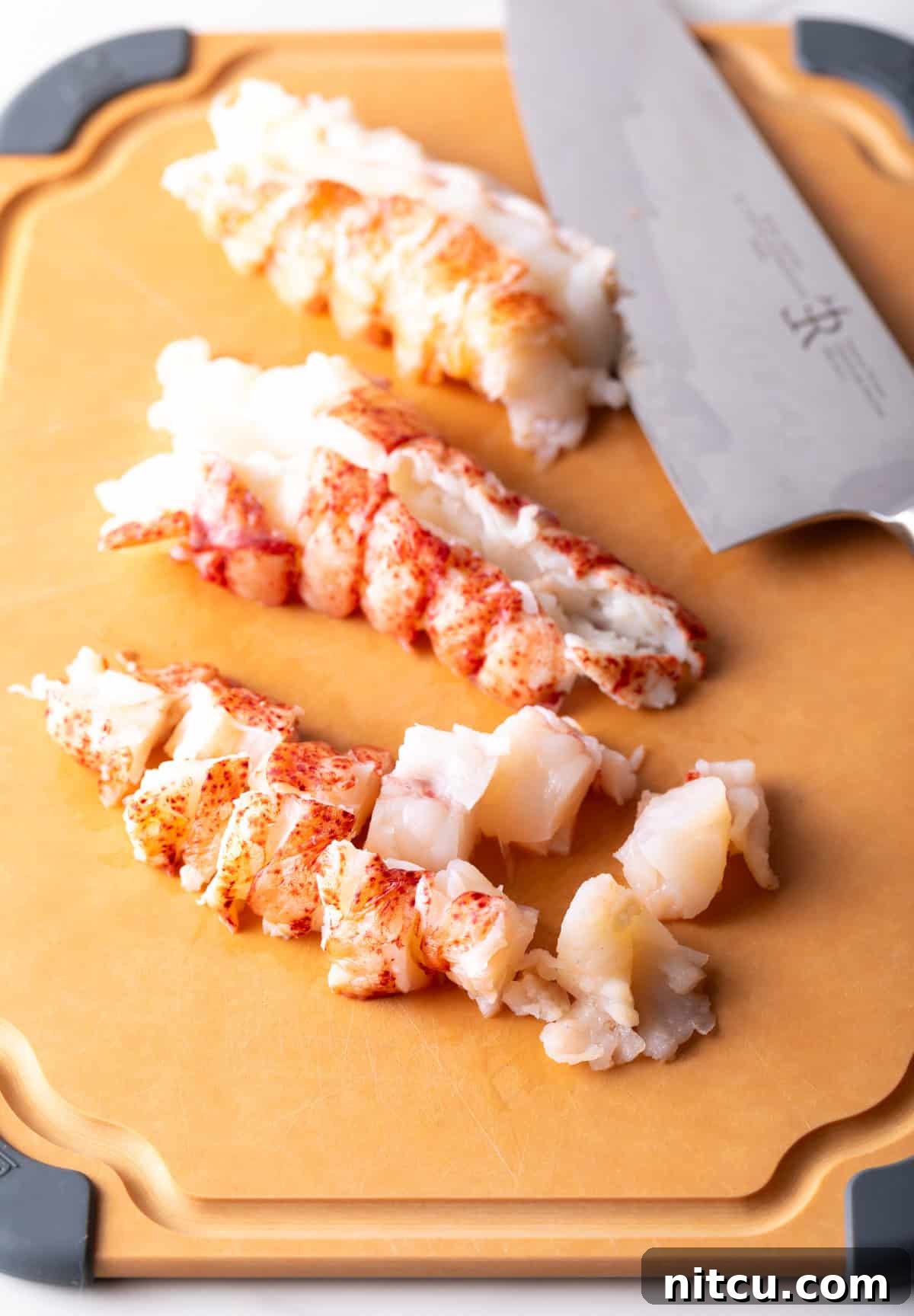 Cooked lobster on a cutting board that is chopped into bite sized pieces for lobster mac and cheese.