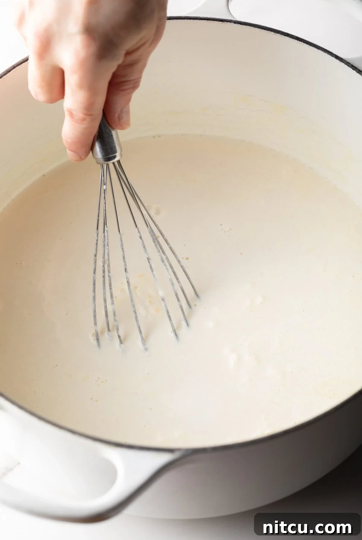 A whisk is whisking the roux and cream mixture for a lobster macaroni and cheese recipe.